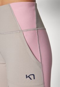Grå og rosa leggings med høy midje, sidelomme og kontraststing. Merkevaren er vist i marineblå.