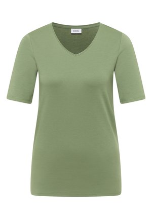 Femme aux cheveux courts bruns portant un t-shirt vert uni à manches courtes et un jean bleu, vue de dos et regardant vers la droite.