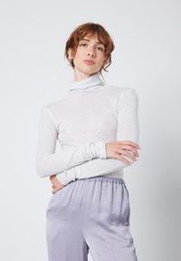 Světle šedý dlouhý rukáv rolák s přiléhavým střihem a měkkou texturou, doplněný volnými levandulovými kalhotami s elastickým pasem.