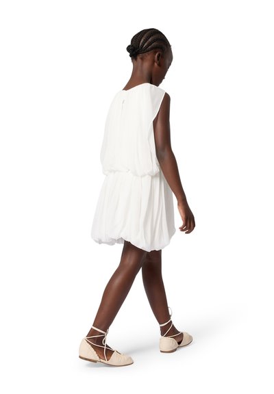 Robe blanche légère avec une silhouette fluide et une taille froncée, assortie à des ballerines beiges avec des brides enveloppantes.