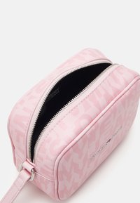 Różowa sztuczna kosmetyczka z zamkiem błyskawicznym, ozdobiona subtelnym wzorem logo i srebrnymi akcentami. Wnętrze jest czarne.