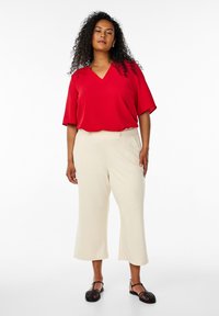 Rode V-hals blouse met brede mouwen, gecombineerd met crèmekleurige brede broekspijpen. Zwarte platte sandalen maken de look compleet. Glad materiaal en een relaxte pasvorm.