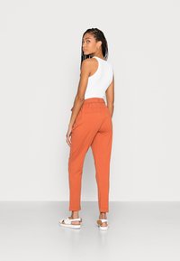 Calças laranja, de pernas afuniladas, com um corte relaxado e cinta elástica. Combinadas com um top branco sem mangas e sandálias brancas.