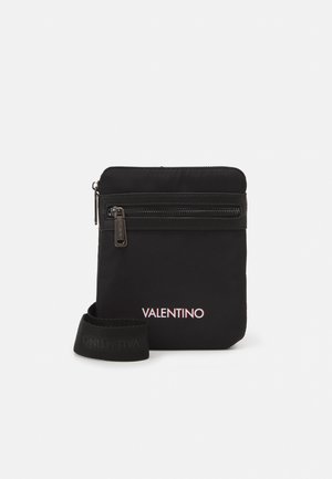 Sac bandoulière rectangulaire noir avec poche zippée à l'avant, logo Valentino en blanc, et sangle réglable en tissu de marque enroulée à la base.