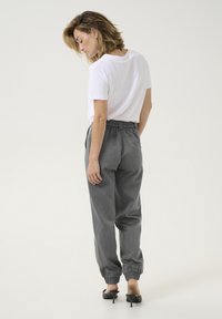 Pantalons de jogging gris, amples, avec une taille élastique, des poches latérales et des poignets froncés, associés à un t-shirt blanc simple.