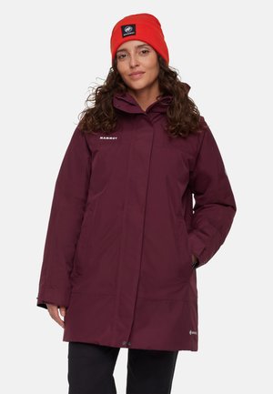 Maroon waterproof jacket with a high collar, zip closure, side pockets, and adjustable cuffs. Paired with an orange knit beanie.