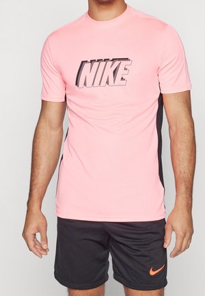 Homme portant un T-shirt Nike rose avec des panneaux latéraux noirs et un short noir avec un logo Nike orange.