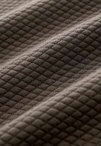Tessuto strutturato di colore marrone scuro con un motivo a diamante. La superficie è morbida e tessuta, con forme geometriche in rilievo e dettagli fini.