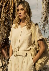 Beige linnen overhemd met korte mouwen, gecombineerd met gestructureerde beige hoge taille broek en een geweven tote tas. Gouden riemaccent.