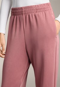 Růžové joggingové kalhoty s elastickým pasem, bočními kapsami a hladkou, jemnou texturou. Navrženy pro pohodlí a volný čas.