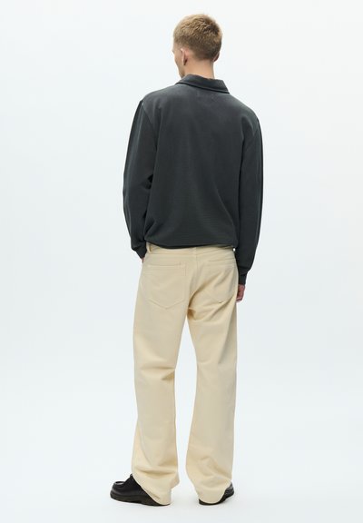 Tmavosivé polo tričko s dlhým rukávom, krémové nohavice so širokými nohavicami a čierne topánky, pohľad zozadu na bielom pozadí.
