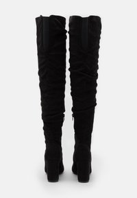 Botas negras hasta la rodilla con textura de ante, diseño fruncido y tacón grueso. Cuenta con una cremallera lateral y un panel elástico en la parte trasera.