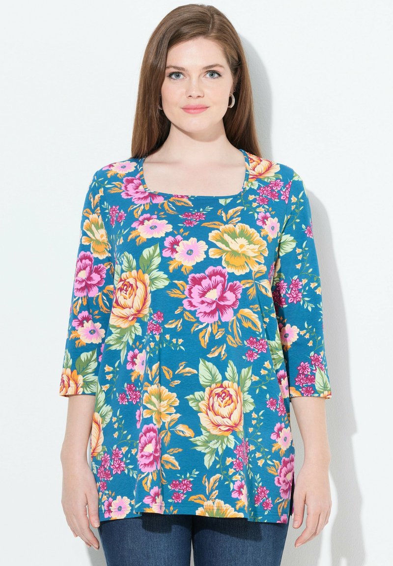 Blumen-Tunika mit quadratischem Ausschnitt, 3/4-Ärmeln und einem blauen Hintergrund mit großen rosa und gelben Blumen sowie grünen Blättern.
