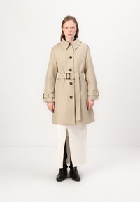 Beige trench coat s širokým límcem, předními knoflíky a páskem v pase. Má dlouhé rukávy s.buttonovými detaily a rovný střih.