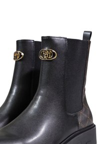 Bottines en cuir noir avec des côtés élastiques et un panneau texturé brun. Présente un accent en logo doré sur le côté extérieur et une semelle épaisse.
