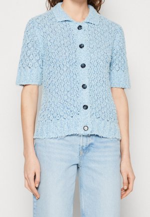 Light blue knitted short-sleeve shirt with a textured pattern, collar, and five dark buttons down the front. Frayed hem detailing.