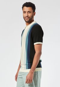 Kortemouw polo shirt in zwart, crème en blauwe strepen. Inclusief een crème kleurige kraag en ribgebreide manchetten, gemaakt van een gladde gebreide stof.