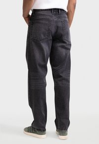 Σκούρο γκρι τζιν με ευθεία γραμμή, διαθέτει δύο πίσω τσέπες και διακριτικό ξεθώριασμα, φορεμένο με πράσινα παπούτσια. Ορατές λεπτομέρειες ραφής.