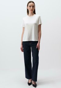 T-shirt bianco a maniche corte, vestibilità rilassata, abbinato a jeans a gamba larga blu scuro e tacchi a punta neri. Tessuto morbido, design minimale.