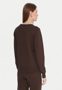 Maglione marrone con scollatura rotonda, polsini e bordo a coste, e una texture liscia, mostrato da dietro con maniche lunghe.