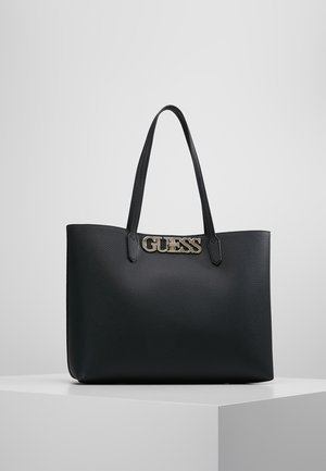 Sort tekstureret læder-tote-taske med dobbelte skulderstropper og guldmetal GUESS-logo foran, vist på hvid piedestal.