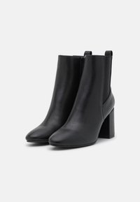 Musta nahkaiset nilkkurit, joissa on sileä pinta, terävä kärki ja paksu korko; varustettu joustavilla sivupaneeleilla ja vetoketjulla.