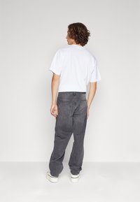 Šedé denimové kalhoty s volnějším střihem, zadními kapsami a stahovací šňůrkou v pase, doplněné o obyčejné bílé bavlněné tričko.