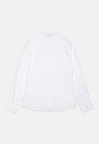 Camicia bianca a maniche lunghe realizzata in tessuto leggero, con colletto a punta, polsini con bottone e dettagli sullo yoke sulla schiena.