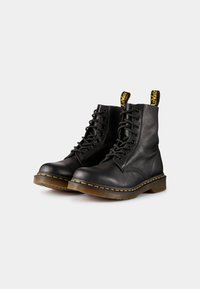 Zwarte leren veterschoenen tot de enkels met een dikke rubberen zool, gele stiksels en trekbanden aan de kraag voor eenvoudig aan- en uittrekken.