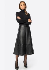 Jupe midi en cuir noir à coupe évasée, avec une texture lisse et des coutures apparentes, associée à un col roulé noir ajusté et des talons.