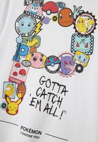 Balta marškinėliai su įvairiais ryškiais Pokémon personažais ir emblema, sudėtais į apvalią figūrą, su tekstu „Gotta catch 'em all!“