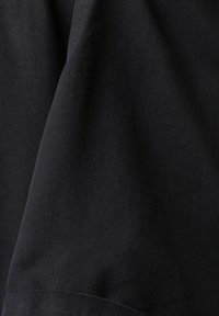 Gros plan d’un tissu noir avec une texture de tissage diagonal et des plis subtils.