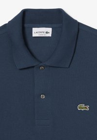 Polo shirt bleu marine en tissu texturé, avec un col en côte, trois boutons et un petit logo de crocodile brodé sur la poitrine.
