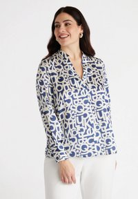 Silk shirt with a navy and cream abstract letter pattern, featuring a collar and long sleeves, shown with white trousers.