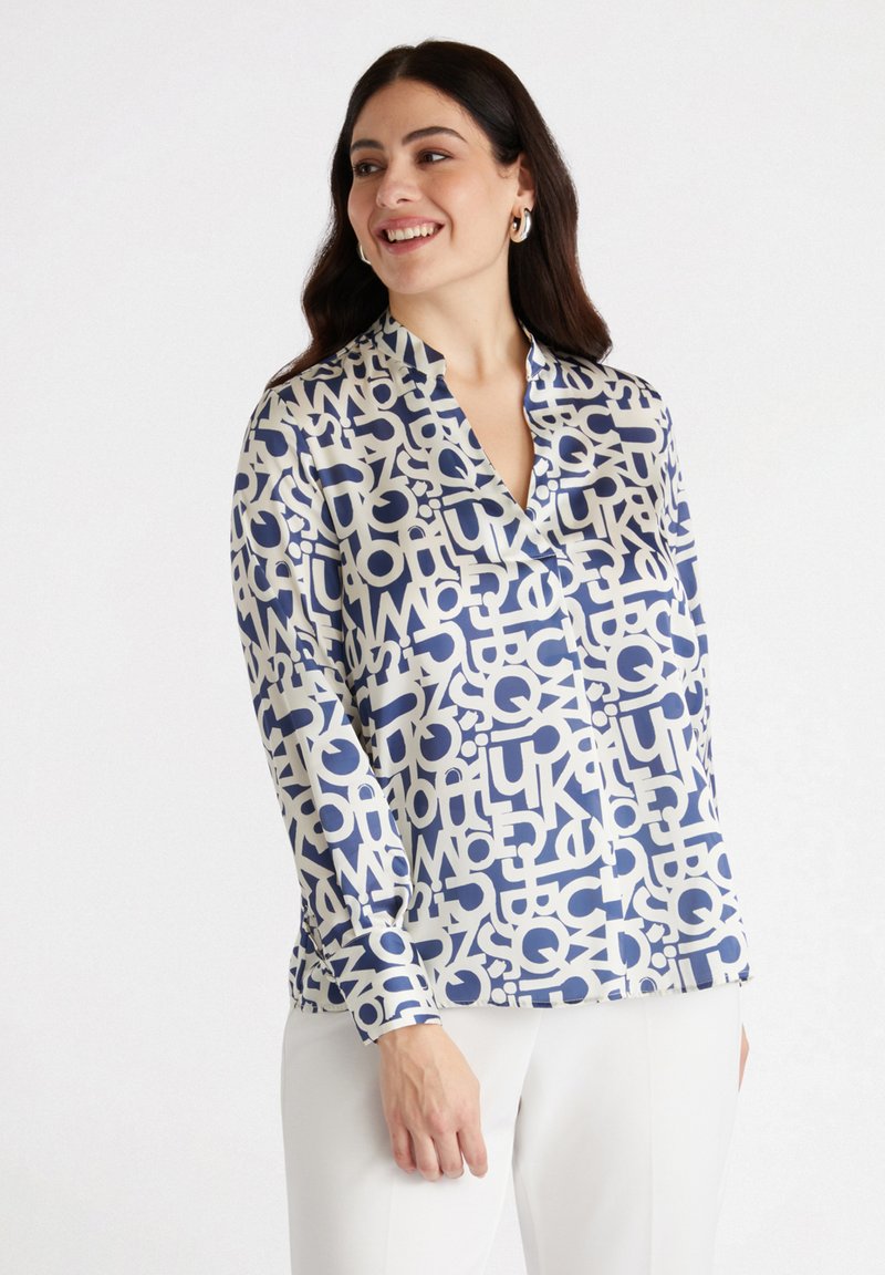 Silk shirt with a navy and cream abstract letter pattern, featuring a collar and long sleeves, shown with white trousers.