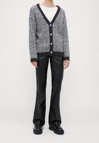 Cardigan grigio e nero con motivo a fantasia, chiusura con bottoni, scollo a V, polsini e orlo a coste, abbinato a pantaloni neri in ecopelle e scarpe chunky.