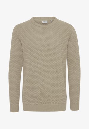 Pull en tricot beige avec motif texturé, col ras du cou, poignets côtelés, associé à un jean en denim bleu et des baskets blanches.