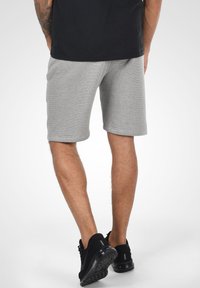 Grijze katoenen shorts met een relaxte pasvorm, tot halverwege de dijen, gecombineerd met zwarte sportschoenen. Soepele textuur en eenvoudig ontwerp.