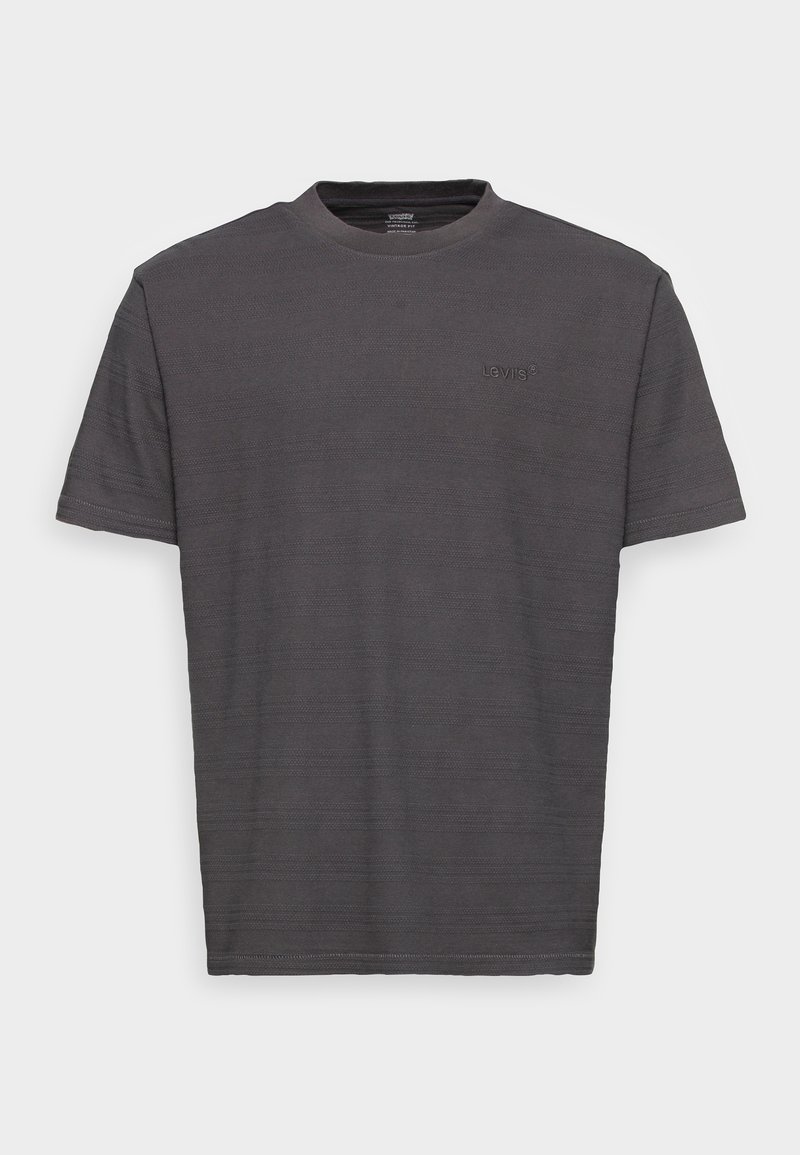 T-shirt gris à manches courtes en tissu texturé, avec un col rond et un logo en relief discret sur le devant.