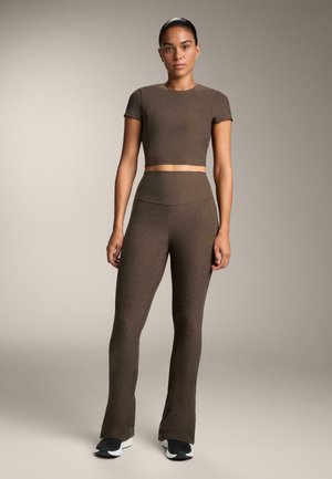 Top corto marrone e leggings a vita alta a zampa d'elefante realizzati in tessuto morbido e testurizzato. Modella che indossa scarpe da ginnastica nere. Design semplice.