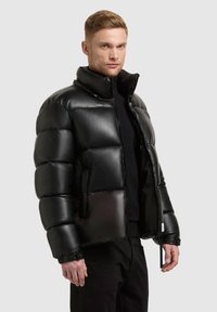 Black puffer jacket with a glossy finish, high collar, and zippered front. Features a boxy silhouette and secured cuffs.