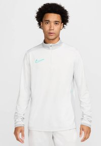 Nike Halbzip-Pullover in Hellgrau mit einer strukturierten Seitenpartie, versehen mit einem türkisfarbenen Logo. Er hat lange Ärmel und einen Stehkragen.