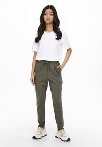 White short-sleeve T-shirt paired with olive green cargo pants featuring pockets and drawstring, worn with beige sneakers.