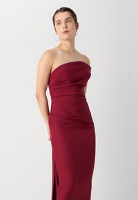 Rochie burgundy fără bretele, cu un corset ajustat, design drapat și fante pe lateral. Construită dintr-un material neted, cu o siluetă elegantă și curată.