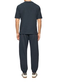 Navy katoenen t-shirt met ronde hals, gecombineerd met bijpassende joggingbroek met elastische manchetten, en witte sneakers met bruine accenten.