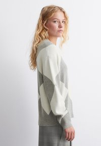 Grau und cremefarbener Pullover im Argyle-Muster aus weichem Material, mit lockerer Passform, langen Ärmeln und gerippten Bündchen.