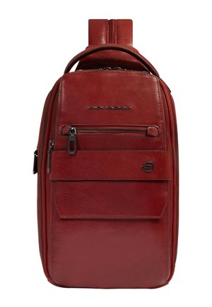 Zaino a tracolla compatto in pelle rossa con tasca frontale con cerniera, manico superiore e tracolla regolabile. Logo in metallo con marchio sul pannello frontale.