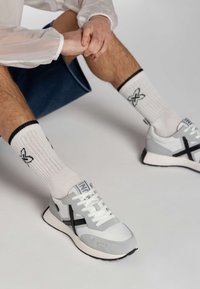 Zapatillas deportivas con una combinación de colores gris claro y blanco, que presentan acentos en negro, materiales texturizados y un diseño de cordones.