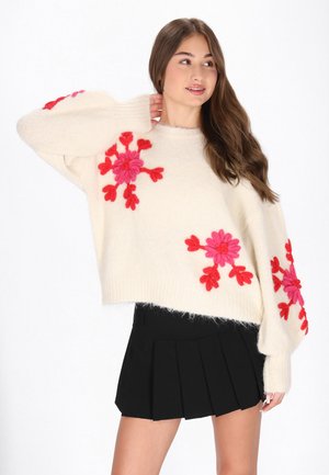 Crème wolken trui met roze en rode bloemen appliqués, cropped ontwerp en geribbelde zoom, gecombineerd met een zwarte geplooide rok.