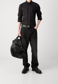 Camisa negra de manga larga con cremallera, jeans negros, cinturón negro, zapatos de cuero negros y un bolso de deporte negro con bordes redondeados.